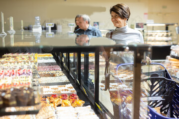 Female customer chooses sweet cakes with interest of the grocery department of supermarket