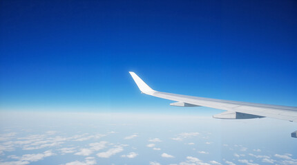 Obraz premium Airplane wing soaring above clouds in clear blue sky 