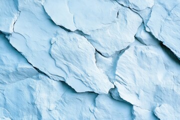Fototapeta premium Light blue rock face texture. Close up view of a textured, fractured rock surface. Pale, almost icy blue hues. Jagged, uneven slabs create a rough, rugged appearance