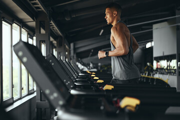Side view of athletic man running on treadmill preforming routine exercise in gym. Sporty male running on track, working on health and fitness at sport club. Sport running concept.