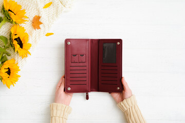 Woman hands holding open empty burgundy leather wallet on wooden table after autumn sale