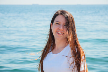 Naklejka premium Smiling young woman enjoying a sunny day at the beach by the ocean. Happy summer days, travel and vacation concept