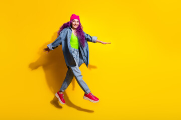 Stylish young woman with purple hair and pink beanie posing joyfully against a vibrant yellow background embracing fashion