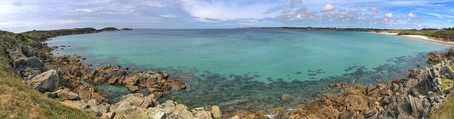 Scenic coastal panorama of a serene turquoise bay with rocky shoreline and sky