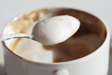 Creamy foam rests on a spoon above a coffee cup