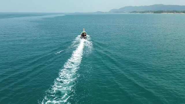 Drone aerial shot of a longtail boat sailing on Koh Lanta Island in the Andaman Sea in Thailand in the bay surrounded by beautiful tropical exotic blue water and rocky island with jungle and waves