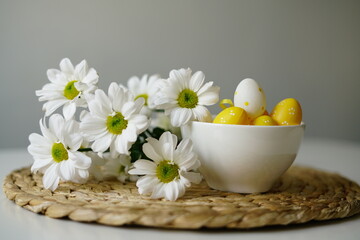 White bowl with yellow Easter eggs and daisies on woven placemat 