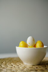 Minimal Easter-themed still life featuring yellow and white polka dot decorative eggs in a clean white ceramic bowl, placed on a woven straw placemat. perfect for illustrating Easter, spring 