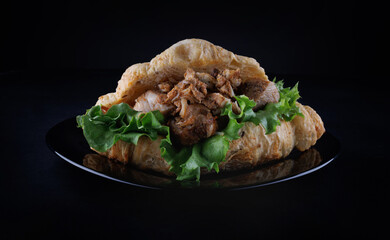 Croissant with grilled chicken meat on a black plate on a black background. Croissant sandwich.