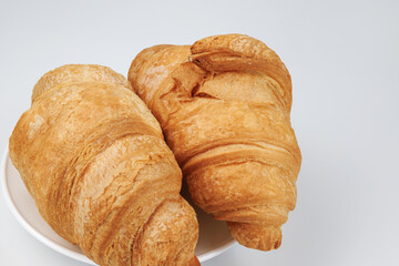 Two fluffy croissants in a white plate on white background.