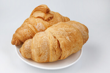 Two fluffy croissants in a white plate on white background.