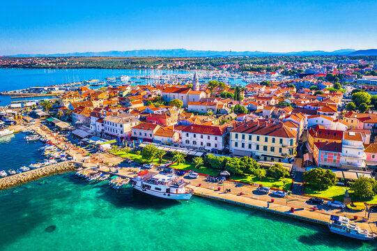 Aerial view of the vibrant waterfront promenade in Biograd na Moru, Dalmatia, Croatia, featuring a lively marina, moored boats, traditional Mediterranean buildings, and the shimmering blue waters