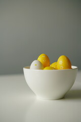 Minimal Easter composition with yellow and white eggs in a glossy ceramic bowl on a white surface. Bright and clean image perfect for spring holidays, decoration, and seasonal design.
