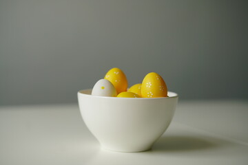 Minimal Easter composition with yellow and white eggs in a glossy ceramic bowl on a white surface. Bright and clean image perfect for spring holidays, decoration, and seasonal design.