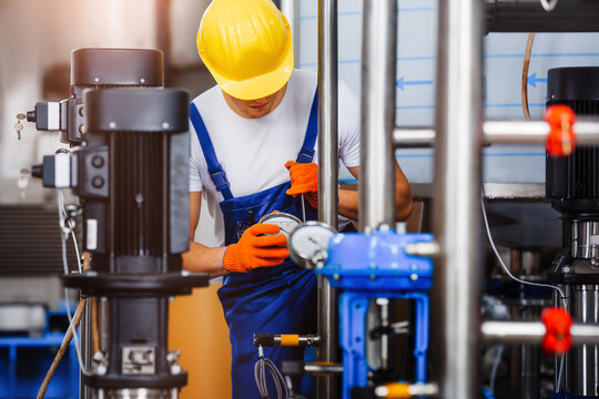 Young worker connects pressure gauge to pipeline system with a wrench. Installation of pipe pressure control system in a chemical production facility.