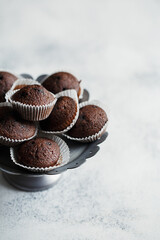 Cake stand with mini chocolate muffins or cupcakes on white concrete background. Side view, close up, copy space