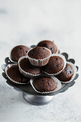 Close up view of cake stand with small chocolate muffins or cupcakes on white concrete background. Side view