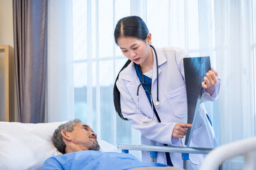 Asian doctor is explaining the x-ray film to senior patient who suffering from lung cancer in the hospital wing for long term smoking disease and care plan surgery program
