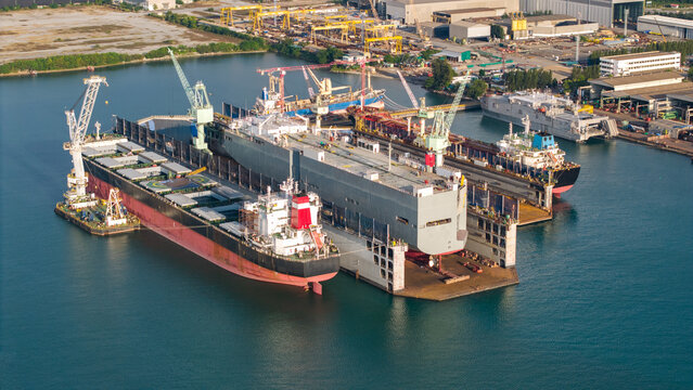 Aerial view of a shipyard repairing a large ship maintenance or repair at floating dock in shipyard both deck crane loading during bring ship in to the dry dock.