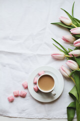 Flat lay with morning cup of coffee, pink candies and bouquet of tulips on white background. Top view, copy space