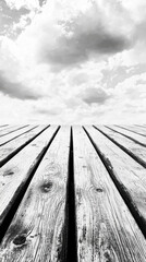 A captivating monochrome photograph showcases a weathered wooden deck extending towards a dramatic sky filled with fluffy clouds creating a stunning perspective.