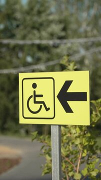 Sign with arrow and wheelchair pictogram in park showing directions of movement of people with disabilities. Providing comfort for inclusive visitors on windy day in vertical video.