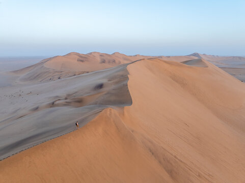 Aerial view of a beautiful sand dune with a man standing on the edge during sunset, Dune 7, Erongo, Namibia.