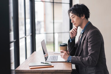 コーヒーを飲みながらノートパソコンを開き仕事をしている日本人男性。