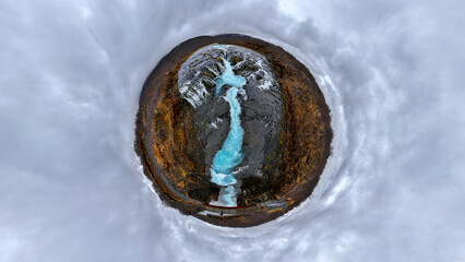 Aerial view of a tiny planet featuring a majestic waterfall cascading into a serene river under a dramatic sky with clouds, Selfoss, Southern Region, Iceland.