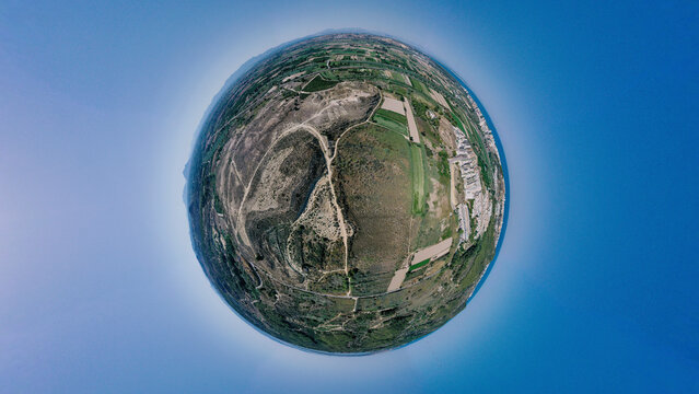 Aerial view of a tiny planet landscape with fields, a road, and a village under a blue sky, Guardamar del Segura, Alicante, Spain.