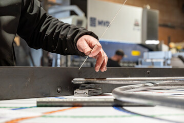 Homme positionnant des pièces métalliques pour assembler un garde-corps, en suivant un plan de dessinateur disposé en dessous.