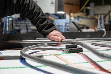 Homme positionnant des pièces métalliques pour assembler un garde-corps, en suivant un plan de dessinateur disposé en dessous.