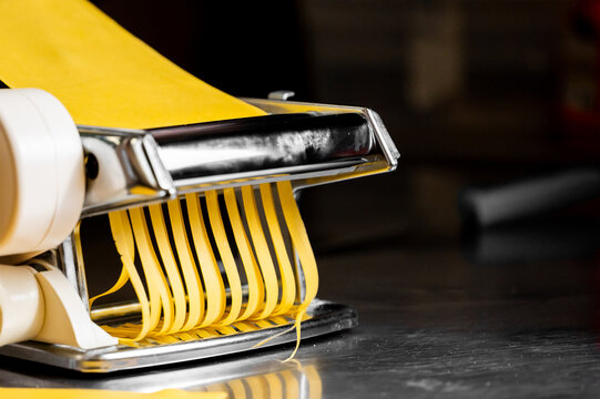 A close-up image of a pasta machine extruding fresh yellow pasta sheets into thin strips, showcasing the artisanal process of pasta making with vibrant colors and shiny surfaces.