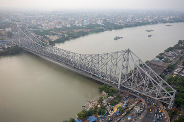 Aerial view of the iconic Howrah Bridge spanning the river with a bustling cityscape and busy traffic, Kolkata, West Bengal, India.