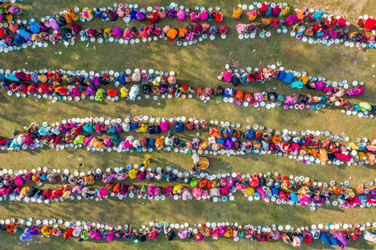 Aerial view of a vibrant majlis public food offering with people in colorful clothing gathered in rows on grass, Saidpur, Rajshahi, Bangladesh.