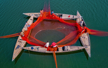 Sariakandi, Bangladesh - 25 December 2021: Aerial view of fishermen using a huge net on a river with wooden boats, Sariakandi, Rajshahi, Bangladesh.