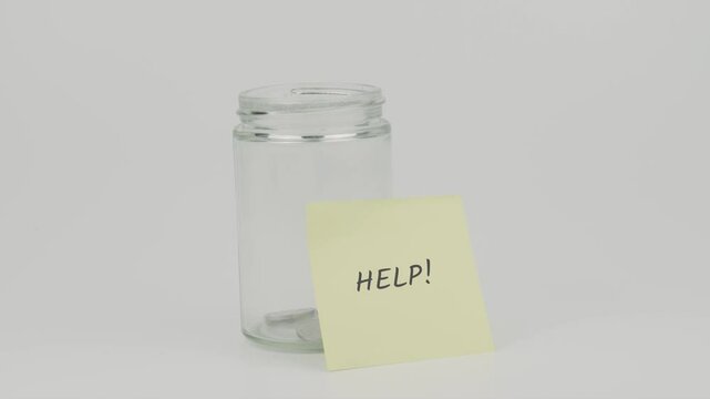 Help text on a yellow note stuck to a jar of coins, with a hand inserting a coin. The image symbolizes the act of saving to provide assistance or support during times of need