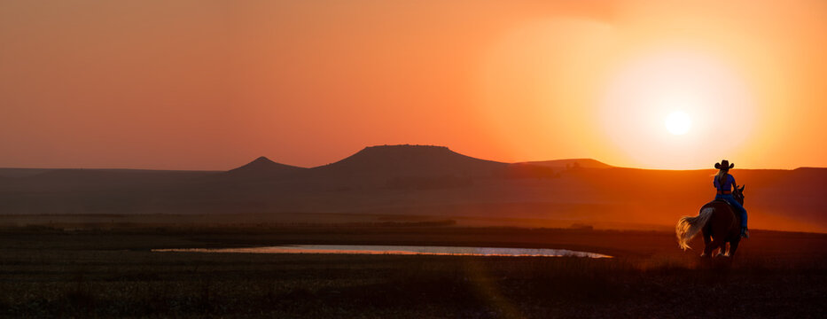 silhouette cowboy in the sunset riding near a water hole in the prairie, American western landscape vista with cowgirl