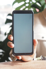 Person holding smartphone in casual indoor setting with greenery