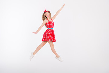 Energetic young woman in a red polka dot dress leaping joyfully against a bright background expressing retro vibes