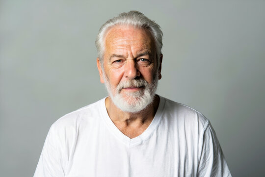 Portrait of an elderly man with white beard and hair in white shirt against light grey studio background, looking calm and content with slight smile.