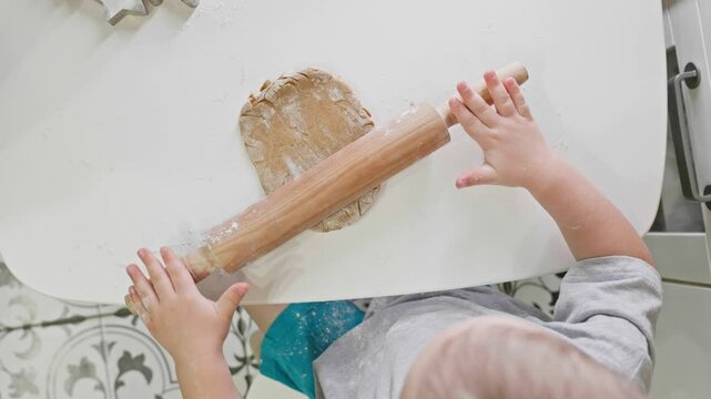 A toddler rolls gingerbread dough in a warm kitchen setting, preparing for holiday cookies. The playful moment highlights the joy of family bonding during seasonal baking. Top view