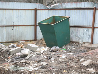 A green open dumpster stands near a solid metal fence