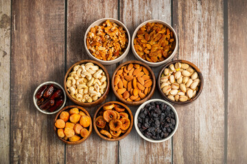 an assortment of dried fruits and nuts arranged in bowls on a white wooden surface, including dates, cashews, almonds, raisins, figs, apricots, and walnuts.