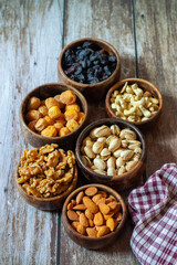  shows six wooden bowls filled with assorted dried fruits and nuts, including raisins, dried apricots, cashews, walnuts, pistachios, and almonds on a wooden table.