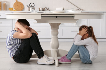Scared little children hiding under table in kitchen during earthquake