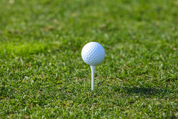 Golf ball on tee ready for first shot,
Close-up image of a white golf ball placed on a tee, set against a green grass,