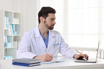 Fototapeta premium Professional doctor working with laptop at white desk in hospital