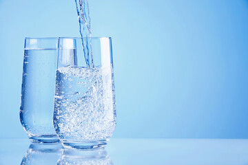 Pouring refreshing soda water into glasses on light blue background, closeup. Space for text