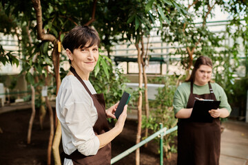 Collaboration between a mature woman and a young colleague in a vibrant greenhouse setting